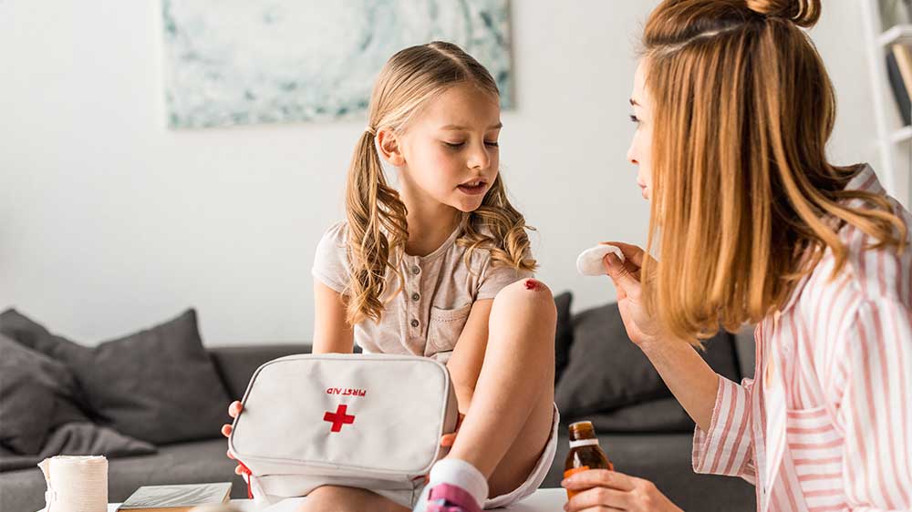 mother treating daughters injured knee with first-aid kit