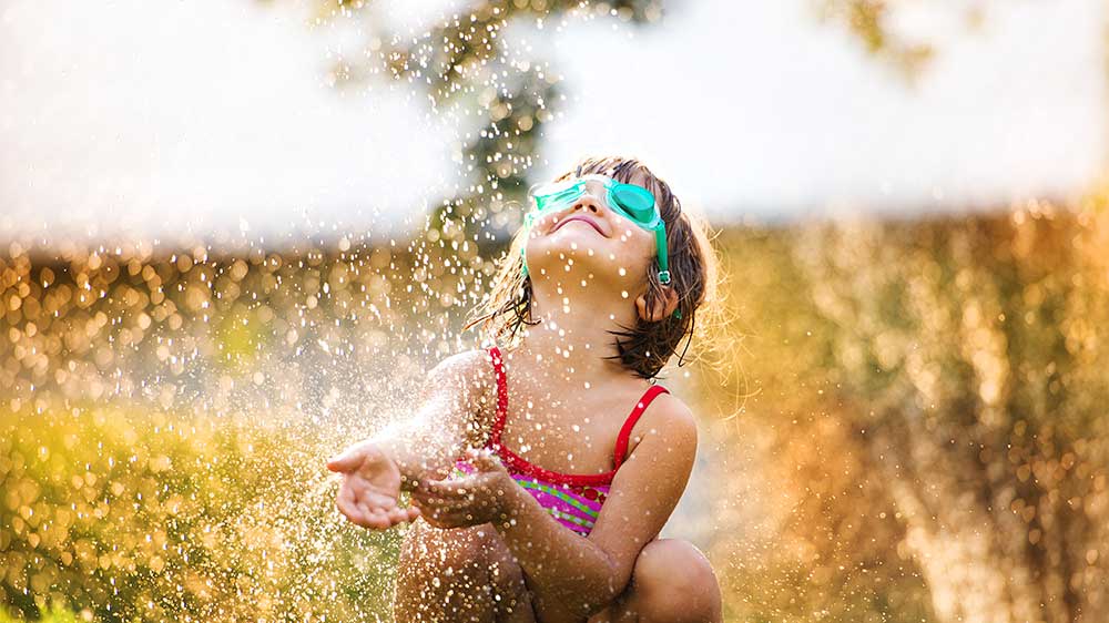 young child playing in sprinklers during summer heat