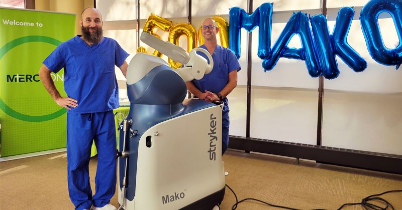 Jason Stanford, DO, and Christopher Egan, DO, pose for a photo with the MAKO robotic arm system.